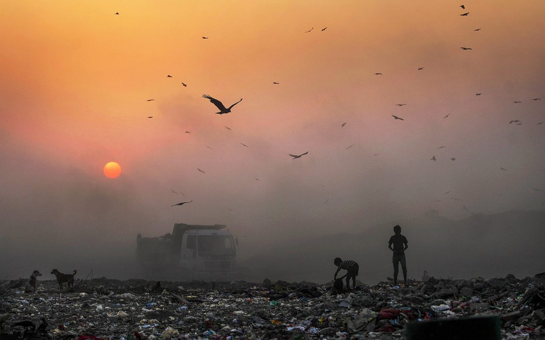 Solen går ner i smogen medan barn letar efter återvinningsbart material på en soptipp i New Delhi, Indien, som tävlar om titeln som världens mest förorenade stad