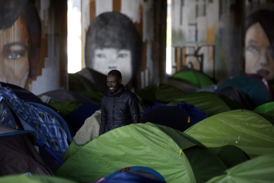 Thibault Camus/AP/TT | En man står bland tälten i ett improviserat migrantläger vid Canal Saint-Denis i Paris.