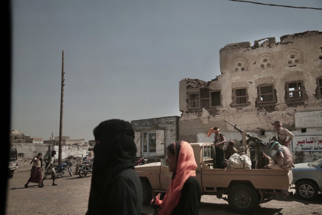 En kvinna promenerar invid militärfordon tillhörande den saudiskledda militäralliansen i hamnstaden Mocha i våras.