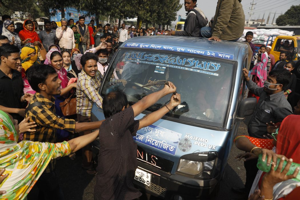 Protesterande textilarbetare i Bangladesh vandaliserar en bil i förorten Savar i Dhaka.