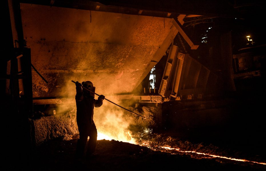 En stålverksarbetare tar bort slagg som lagt sig på det smälta råjärnet som rinner ut från masugn 4 på SSAB i Oxelösund.