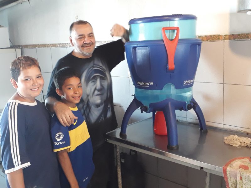 Julio Esquivel, som driver soppköket för barn i kåkstaden La Cava, visar tillsammans med två av barnen upp den vattenrenare som blivit ett stort lyft för området.