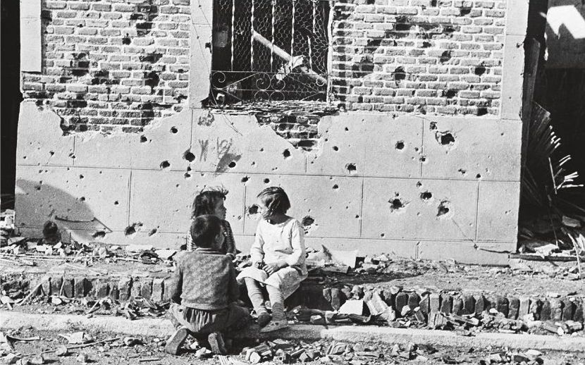 Barn diskuterar något på en sönderskjuten gata under inbördeskriget i 30-talets Katalonien.