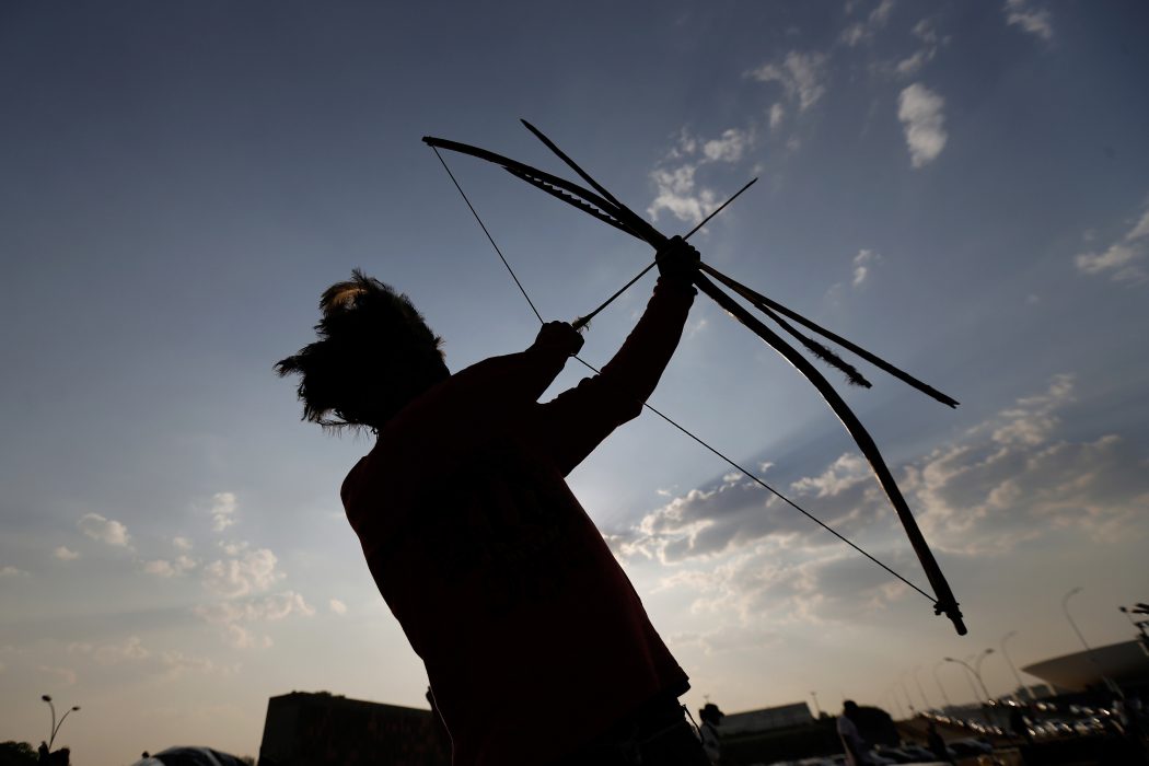 A young Indian of the Guarani Kaiowa tribe plays with traditional bow and arrow as members of the tribe set up camp in front of the headquarters of the Brazilís Supreme Court, in Brasilia, Brazil, Wednesday, Oct. 15, 2014. Around one hundred Guarani Kaiowa Indians from the state of Mato Grosso do Sul, are demanding the demarcation of their lands and the end of violence against indigenous leaders. (AP Photo/Eraldo Peres) En ung man som tillhör guaraní-kaiowáfolket spänner en traditionell pilbåge utanför högsta domstolen i Brasilia, Brasilien, under en demonstration där guaraní-kaiowáfolket kräver att staten ska ge dem tillbaka sina landområden