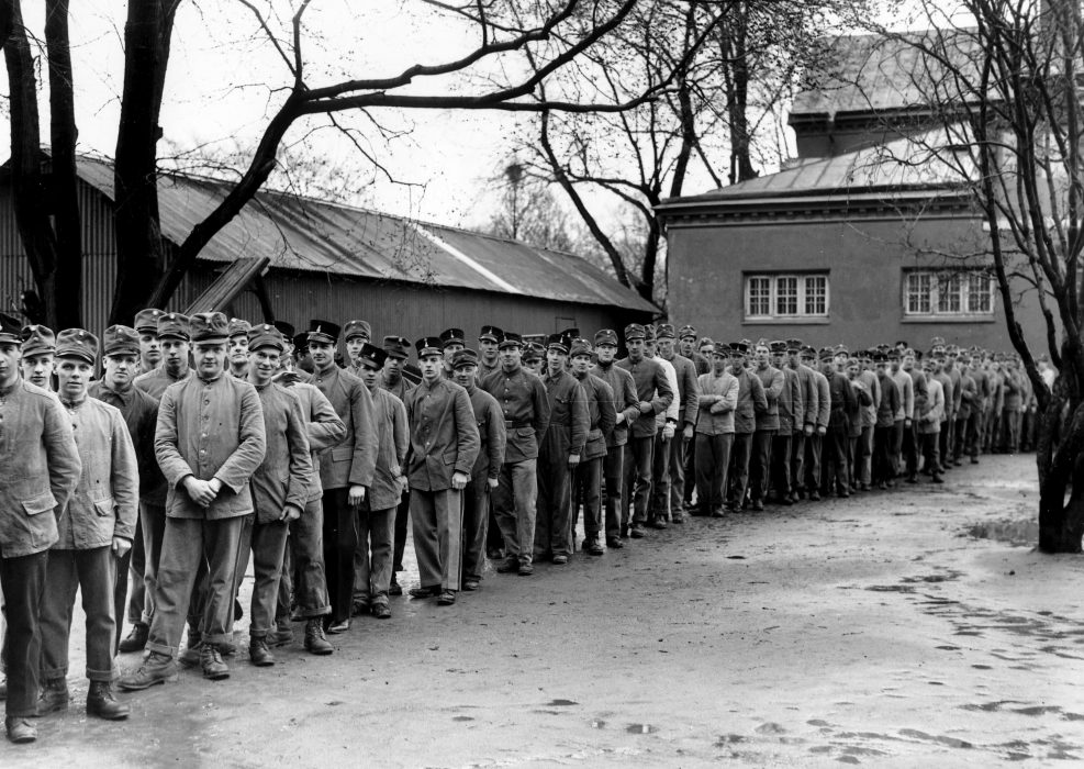 Soldater i grötrock köar till lunchen vid ett regemente på 1930-talet.