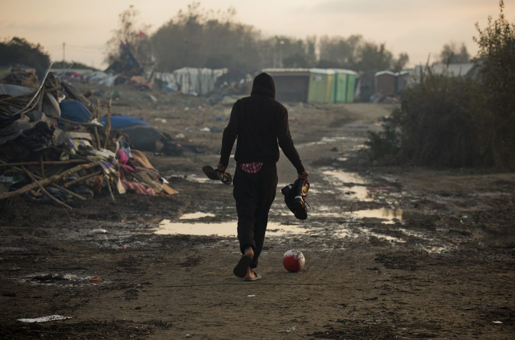 A migrant kicks a ball as he past tents destroyed in the makeshift migrant camp known as "the jungle" near Calais, northern France, Friday, Oct. 28, 2016. Thousands of migrants dispersed this week from the now-torched camp they had called home in Calais are struggling to adapt to unfamiliar surroundings in towns and villages throughout France. (AP Photo/Emilio Morenatti)