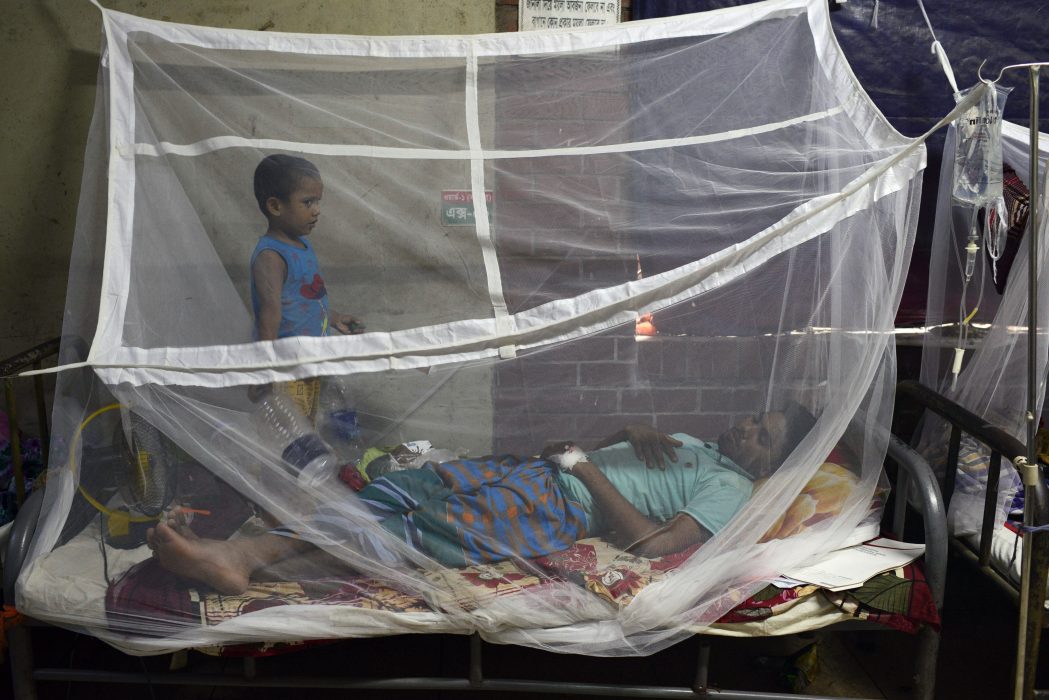 Ett barn står vid sin pappa som behandlas för denguefeber i Dhaka.