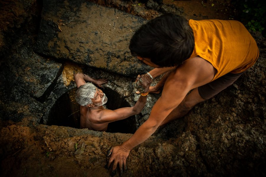 54-årige Kaverappa från Bangalore i Indien hjälps upp ur latrinhålet han håller på att tömma av en kollega.