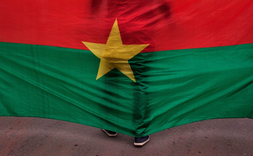 En man står vid en burkinsk flagga under en minnesceremoni för offren för en attack i landets huvudstad Ouagadougou 2016.