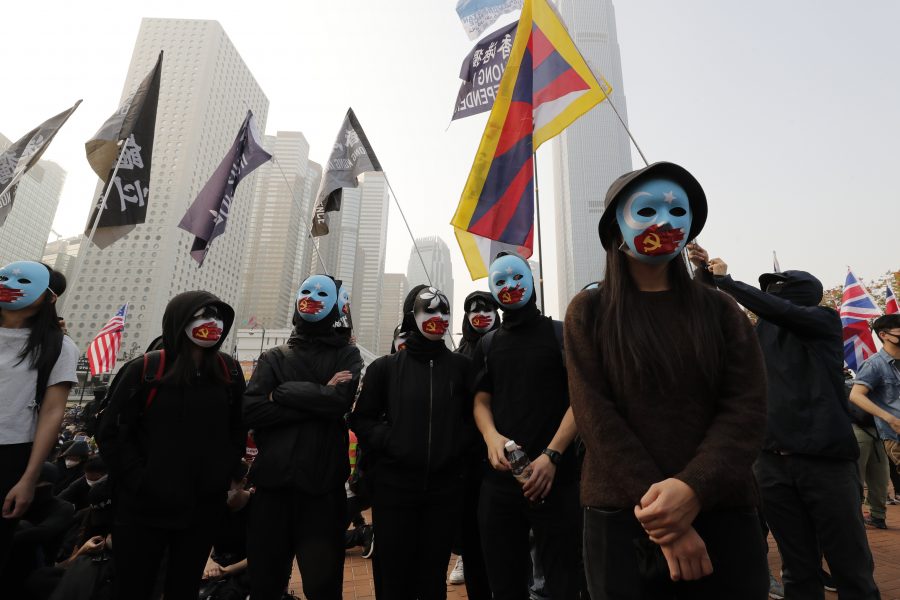 Människor vid demonstrationen bär målade masker, där uigurernas ljusblå separatistflagga täcks av en hand målad som Kommunistpartiets symbol.