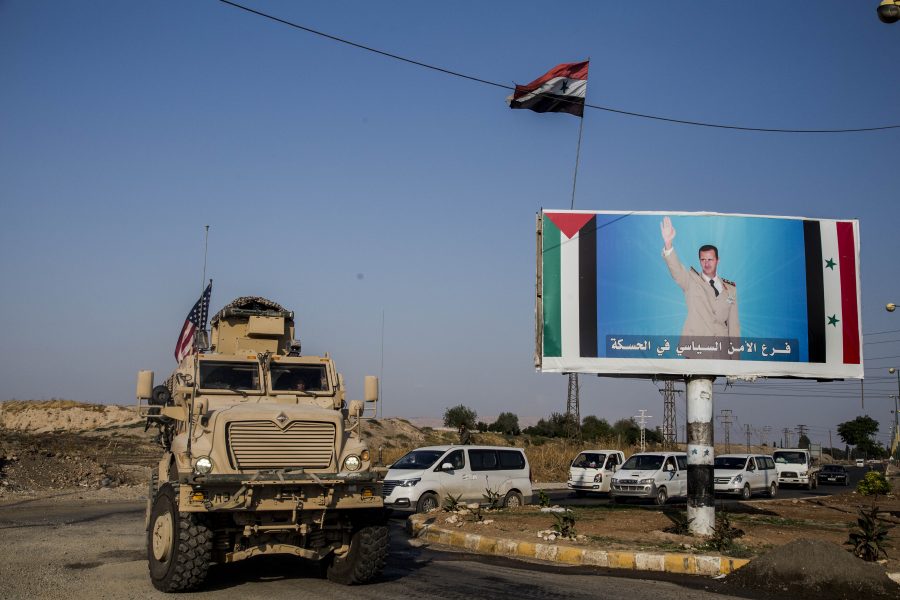 En amerikansk militärkonvoj i staden Qamishli i norra Syrien bredvid en bild av landets president Bashar al-Assad.