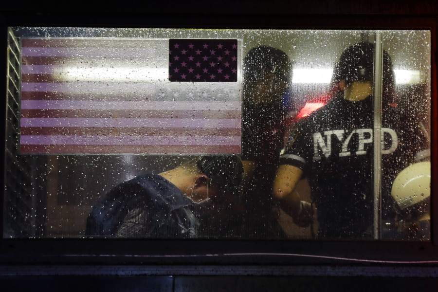 En polis talar med en gripen person i en buss under protesterna i New York.