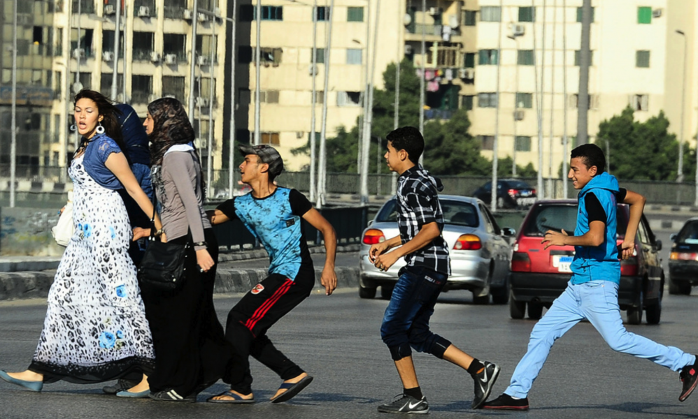 En ung man, med sina vänner i släptåg, tafsar på en kvinna då hon går över en gata i Kairo.