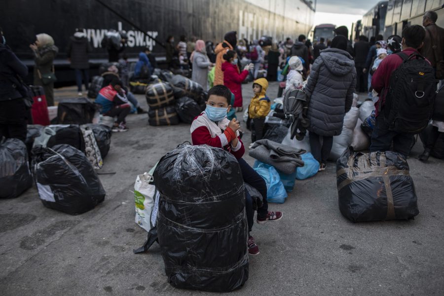 Flyktingar bär mask för att undvika smittspridning när de anländer från öarna till Piraeus, en hamn utanför Aten.