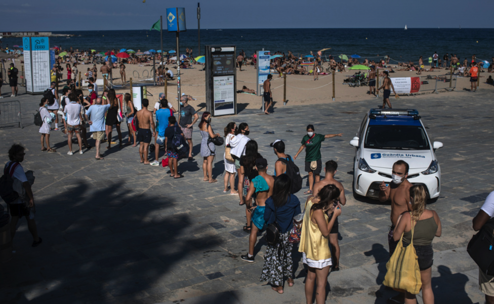 Semesterfirare köar till en strand i Barcelona som stängts av polis på grund av trängsel den 18 juli.
