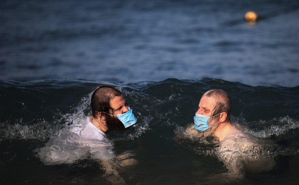 Två män simmar med munskydd i Tel Aviv tidigare i juli.