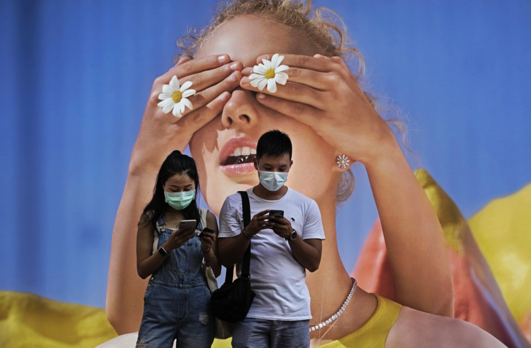 Ett par med ansiktsmask framför en stor affisch i Hongkong.