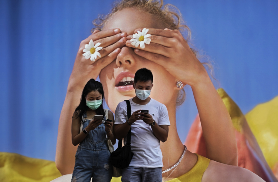 Ett par med ansiktsmask framför en stor affisch i Hongkong.