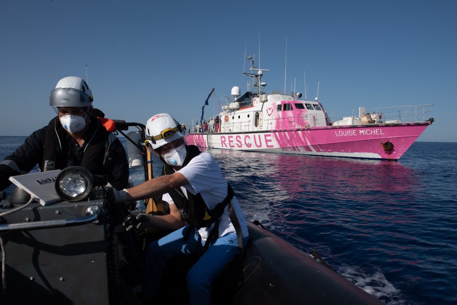 Louise Michel i bakgrunden och besättning ombord på en mindre båt tillhörande teamet ombord på Sea-Watch4 i lördags, när de flyttade 150 flyktingar från den mindre Louise Michel till sitt större fartyg.