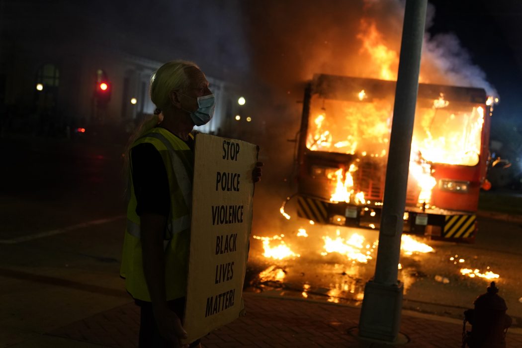 En demonstrant står framför en brinnande sopbil utanför Kenoshas domstolsbyggnad på måndagkvällen.