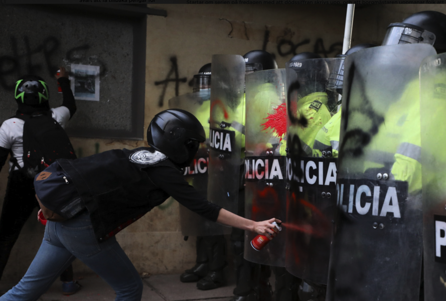En demonstrant sprayar färg på kravallpolisernas sköldar i Bogotá.