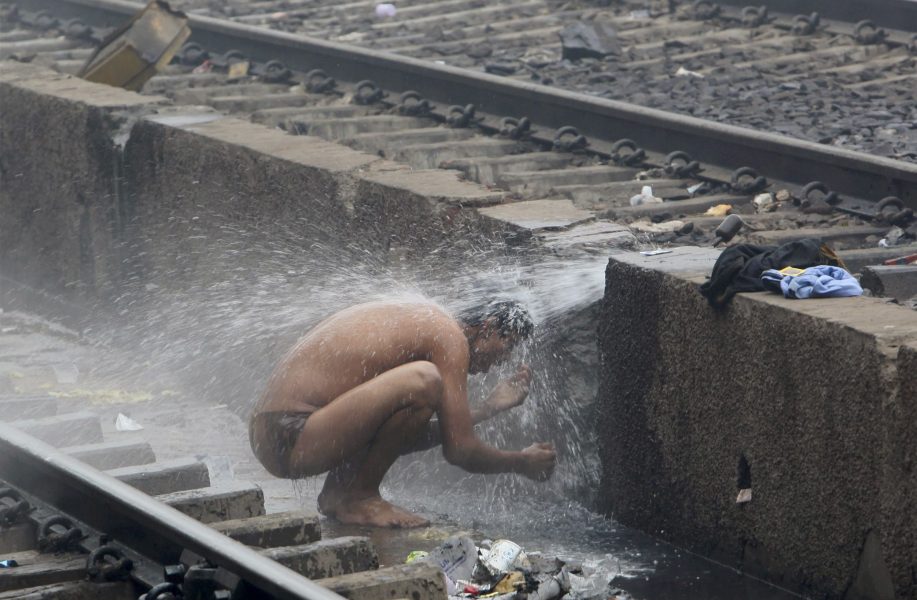 En man tar en dusch vid järnvägsspåren i New Dehli.