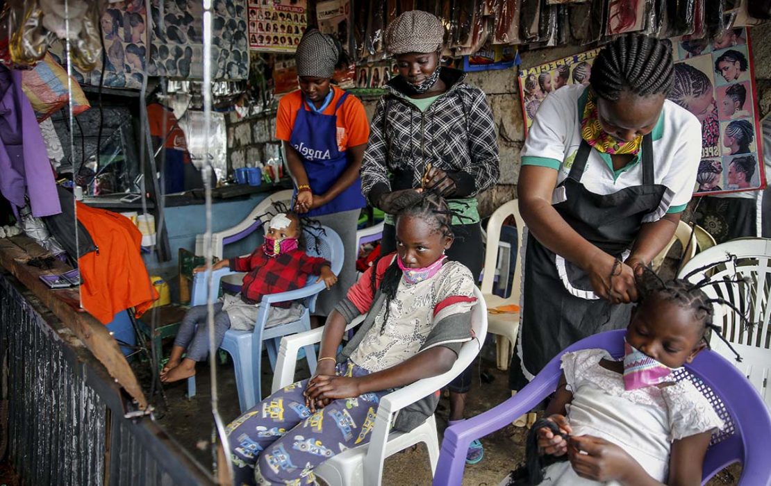 Smitttspridningen av Covid-19 och andra virus kan inte stoppas så länge fattiga tvingas ut och jobba för att överleva. Därför föreslår FN nu basinkomst. På bilden: Gettrueth Ambio, Jane Mbone, och Hamida Bashir, får håret stylat i samma form som nya coronaviruset, på salong Mama Brayo Beauty Salon i Kiberas slum slum i Nairobi, Kenya. Foto: Brian Inganga/AP/TT