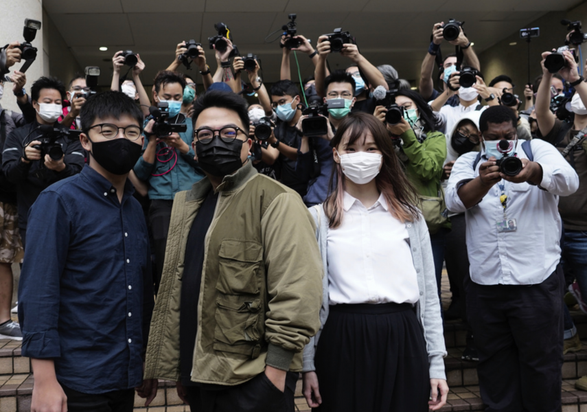 Joshua Wong (till vänster), poserar framför domstolsbyggnaden tillsammans med aktivisterna Ivan Lam och Agnes Chow, som också står inför rätta.