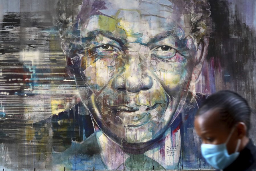 En kvinna i ansiktsmask passerar en muralmålning av Nelson Mandela.