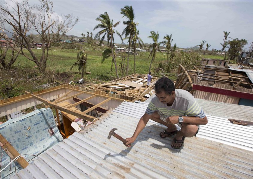 En man lappar ihop sitt hus efter den förödande cyklonen Winston, som drabbade Fiji 2016.