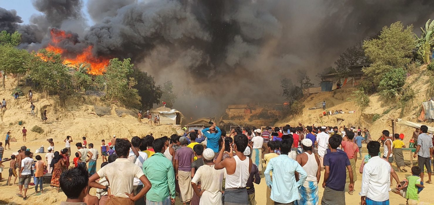 Människor ur folkgruppen rohingya framför röken och lågorna efter branden som blossat upp i flyktinglägret Balukhali i södra Bangladesh.