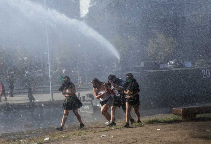 Demonstranter springer från polisens vattenkanon i Chiles huvudstad Santiago på den internationella kvinnodagen den 8 mars.