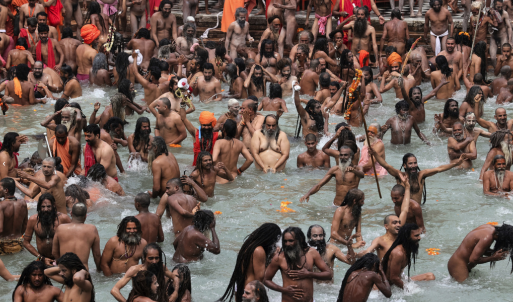 Troende – de flesta utan munskydd – firar den hinduiska högtiden kumbh mela genom att ta renande bad i floden Ganges.