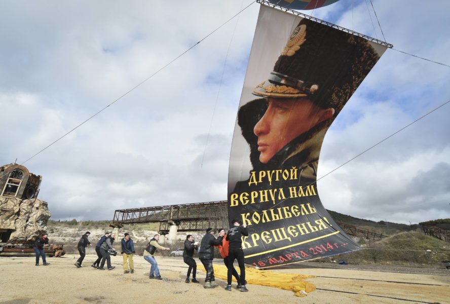 I staden Sevastopol på ukrainska Krimhalvön monteras en flagga med Rysslands president Vladimir Putin, med texten "En annan gav oss åter dopets vagga", på sjuårsdagen av den ryska annekteringen av Krim i mars i år.