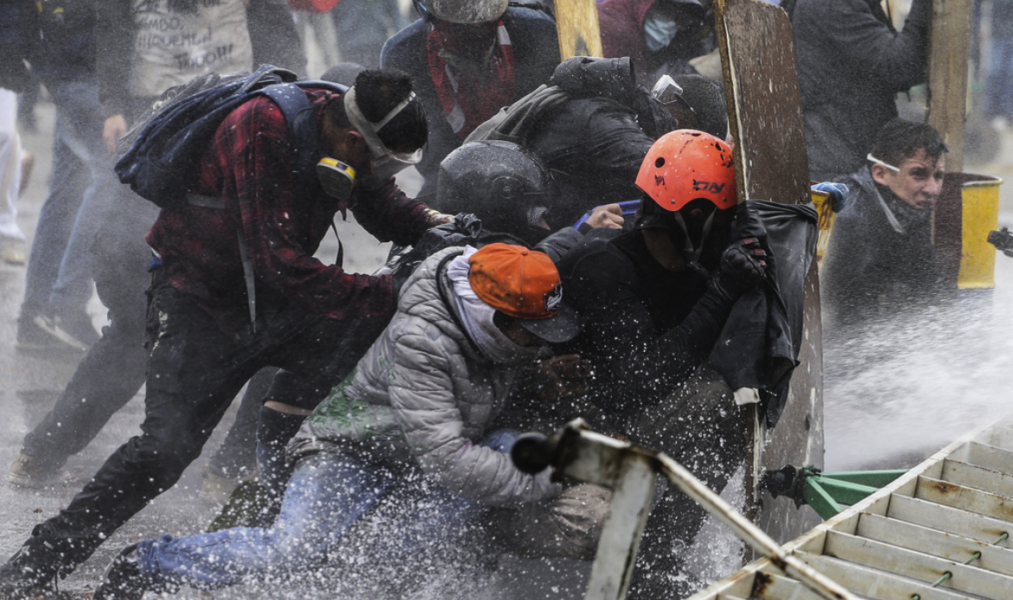 Demonstranter tar skydd för polisens vattenkanoner utanför Colombias huvudstad Bogotá under fredagen.