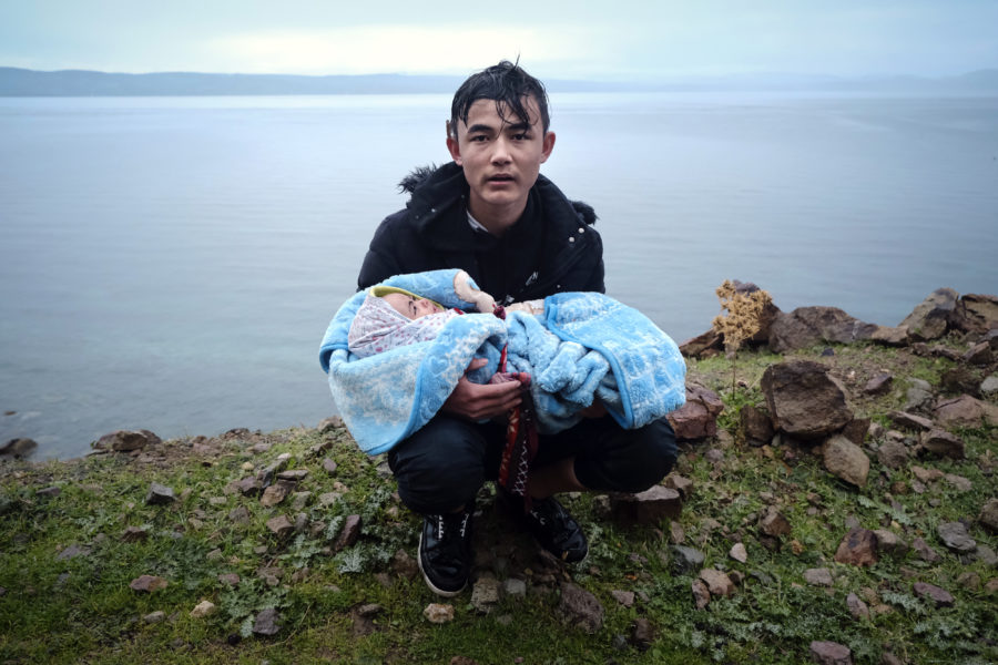 En flykting som just korsat egeiska havet håller i en bebis, som också var ombord på den lilla båten.
