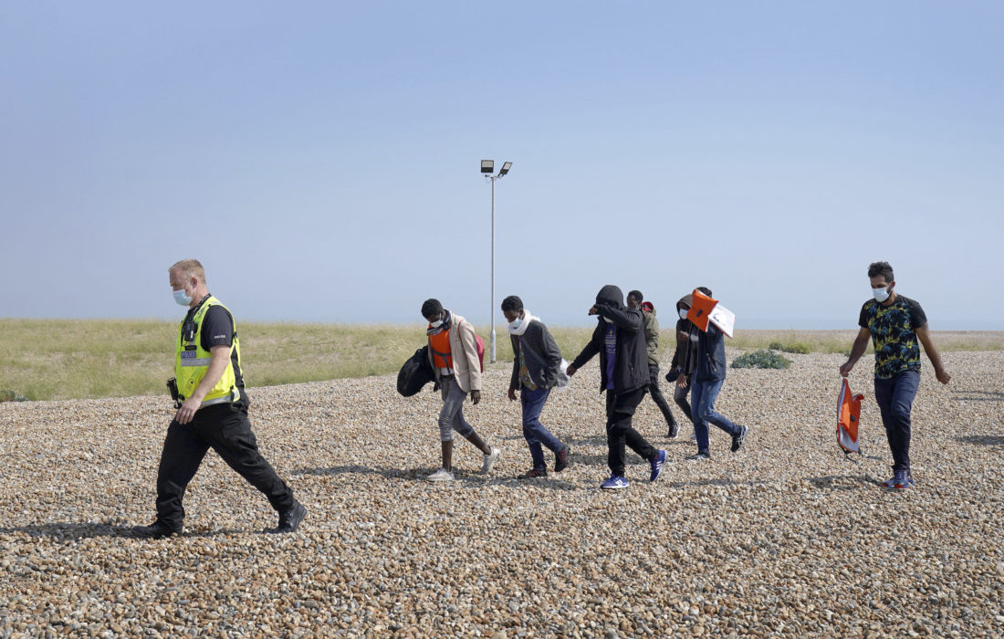 Polis eskorterar en grupp människor som tros ha anlänt sjövägen till Dungeness i södra England.
