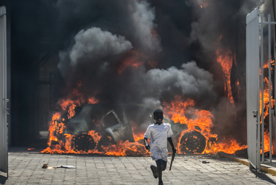 En pojke flyr från en bilhandel som satts i brand under demonstrationer i Port-au-Prince i mars i år.