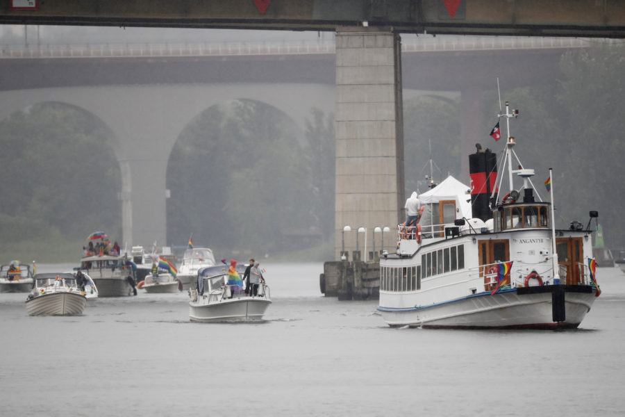 Båtar i ösregn tar sig ut i en prideparad från Årstaviken, under Liljeholmsbron, mot Riddarfjärden i Stockholm.