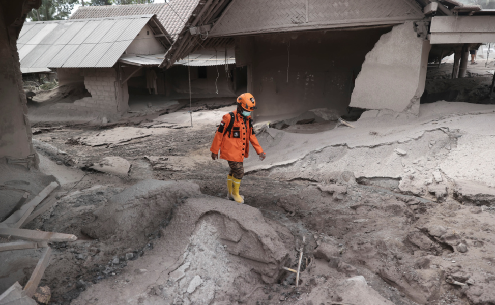 Räddningspersonal passerar framför förstörda hus efter lördagens vulkanutbrott på ön Java i Indonesien.