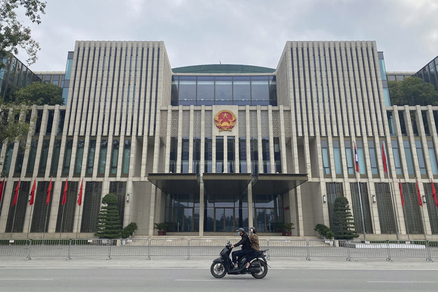 En mopedist med passagerare passerar nationalförsamlingen i Hanoi.
