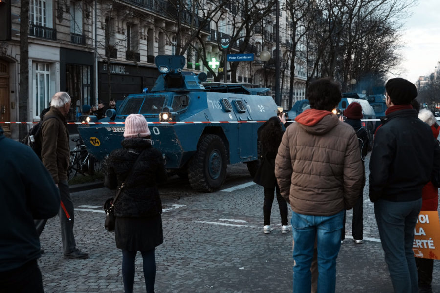 Människor i Paris står framför ett av polisens militärfordon.