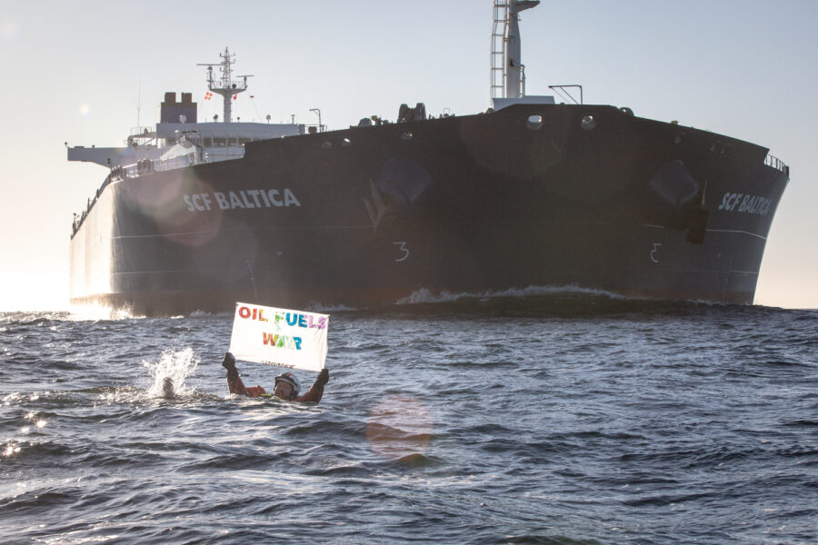 Aktivist från Greenpeace simmar i vattnet framför oljetankern SCF Baltica med budskapet "Olja göder krig".