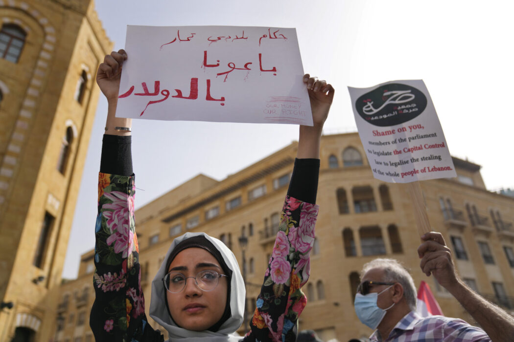 Protest i Beirut i maj, en ung kvinna håller upp en skylt på arabiska där det står "Våra makthavare sålde oss i dollar"