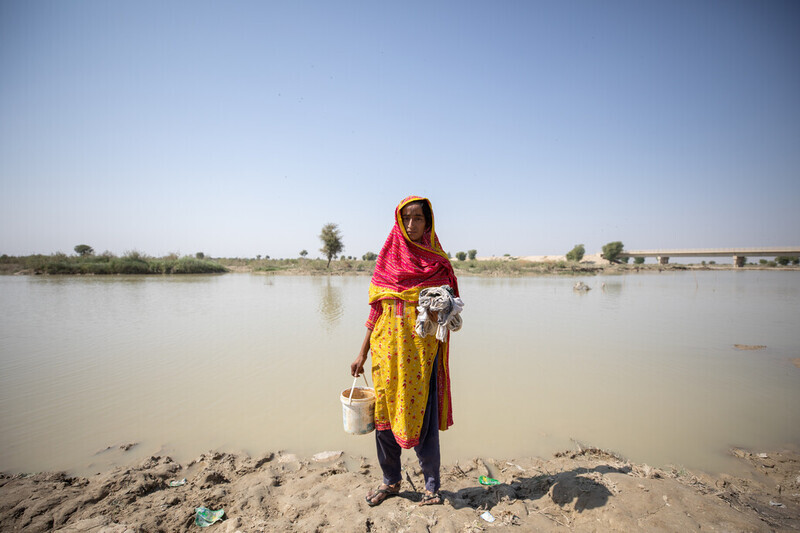 En kvinna tvättar sina kläder i det stagnerade flodvattnet.