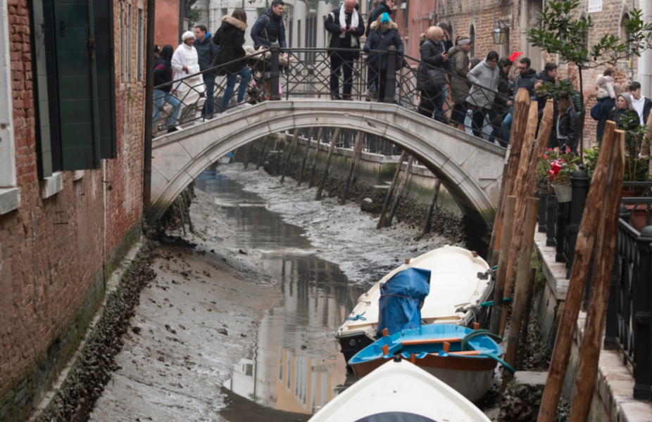 Turister på en av Venedigs många broar inspekterar de torra kanalerna den 21 februari.