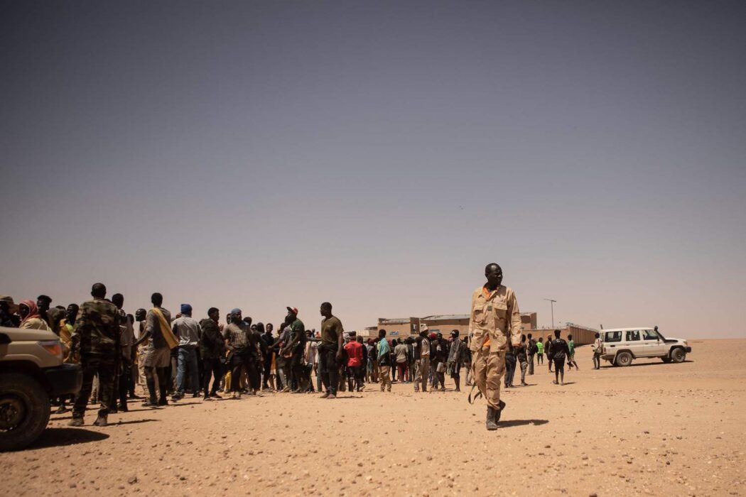 Soldater har ett vakande öga kring samlade migranter i det nigeriska gränssamhället Assamaka.