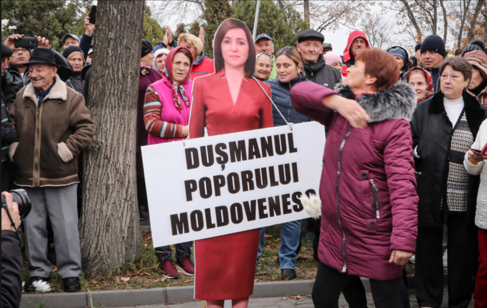 En kvinna slår en kartongmodell av Moldaviens västvänliga president Maia Sandu med en skylt som lyder "Det moldaviska folkets fiende".