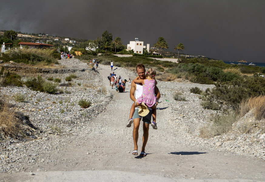 En man bär sin dotter i famnen, på flykt från en av de stora bränder som de senaste dagarna rasat på den grekiska ön Rhodos.