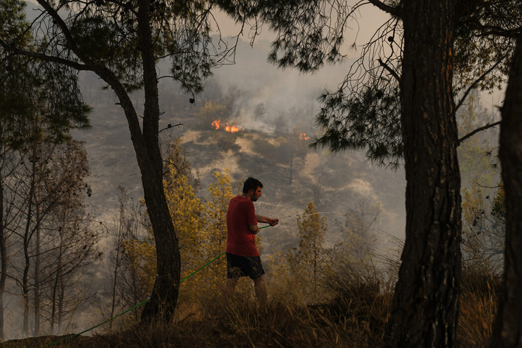 En man försöker släcka en brand väster om Greklands huvudstad Aten.